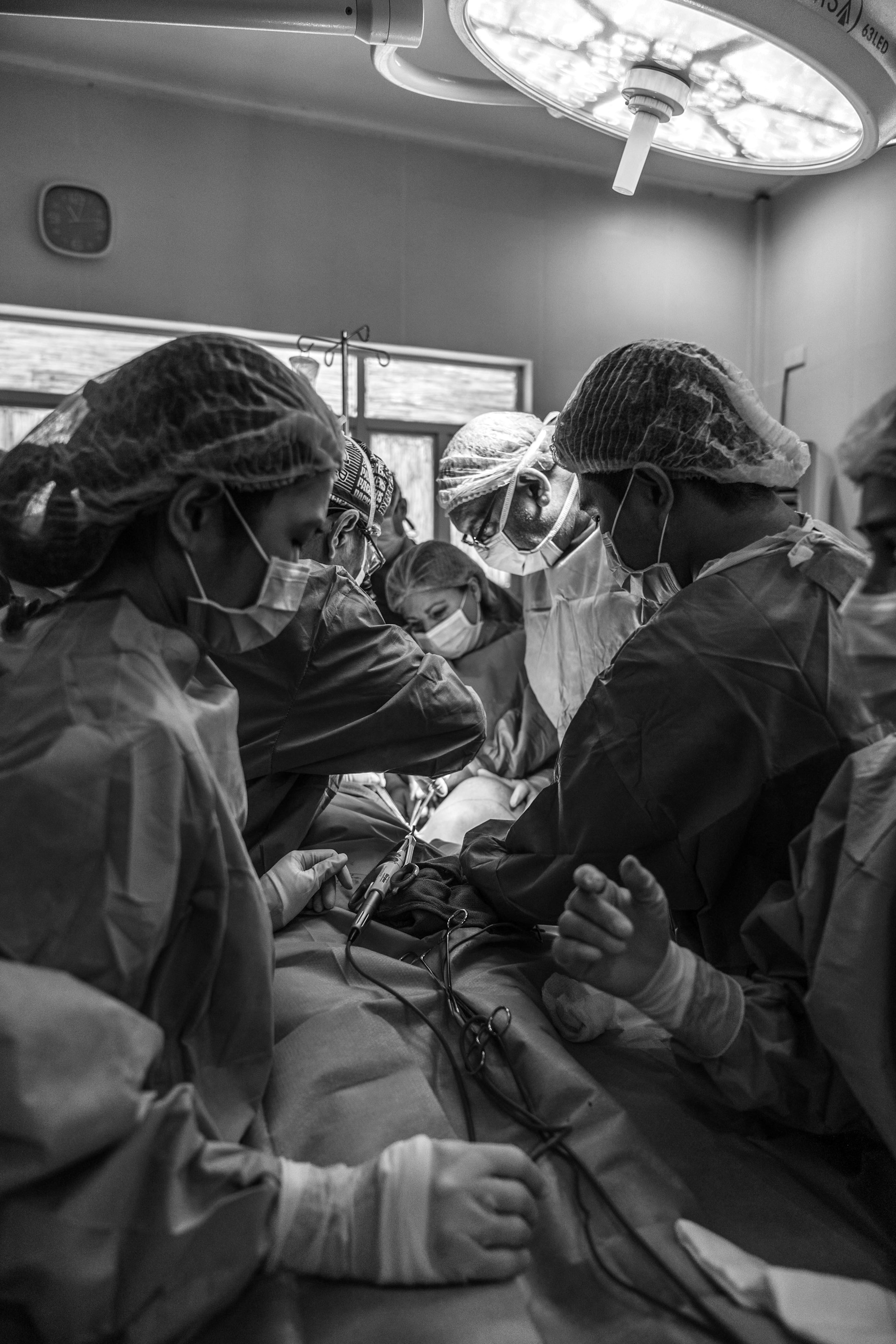 Active ICU room, many doctors and nurses wearing masks standing over a patient